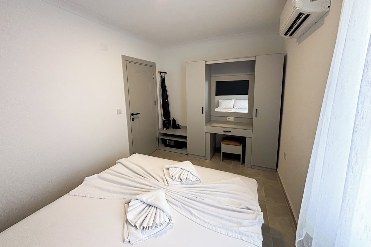 A hotel room with a bed, a wardrobe, a mirror, and an air conditioning unit.