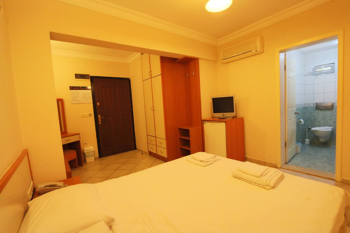 A hotel room with a bed, a television, a bathroom with a toilet and sink, and a wardrobe.