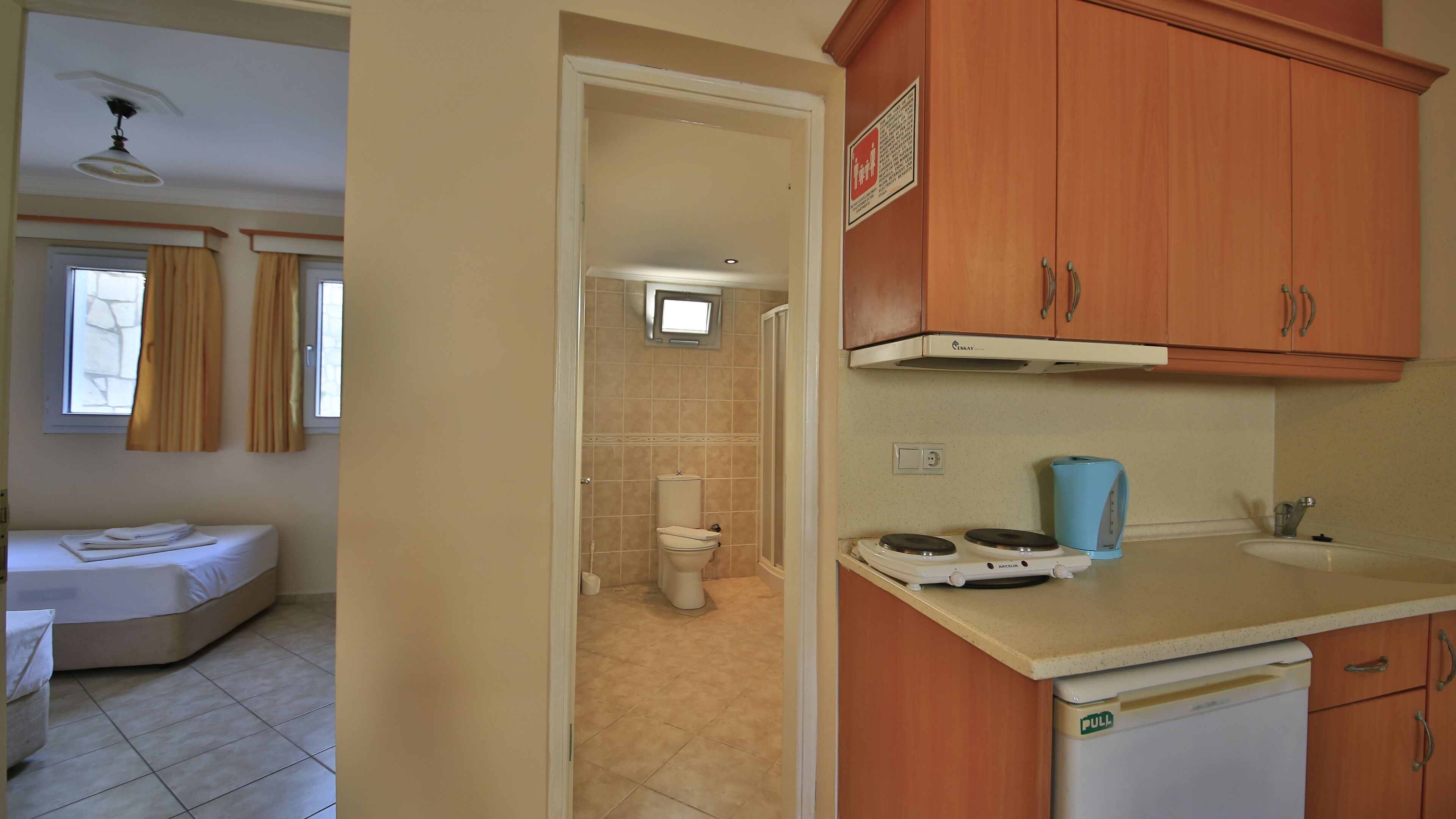 A room with a bed, a bathroom with a toilet and shower, and a kitchenette with a stove and sink.