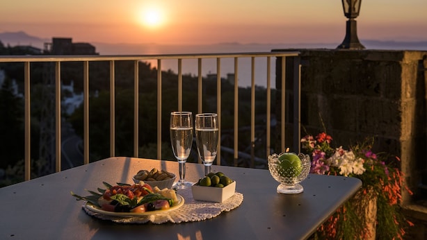 A table with two glasses of water, a bowl of olives, and a bowl of fruit on a balcony overlooking a sunset. - Villa Carolina Country House (Sorrento)