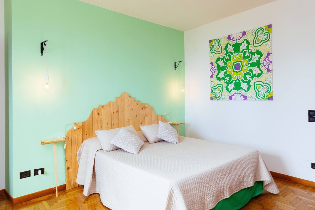 Une chambre à coucher avec une tête de lit en bois, un lit avec une literie blanche, un mur vert et un élément décoratif mural.