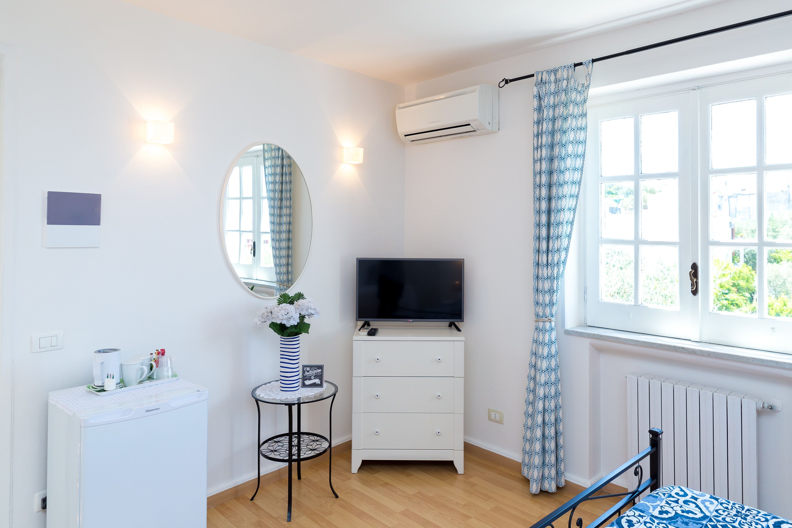 A bedroom with a bed, a TV, a dresser, a radiator, and a window with curtains.