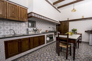 Een keuken met houten kastjes, een betegelde achterwand, een centraal eiland en een eetgedeelte met een tafel en stoelen.