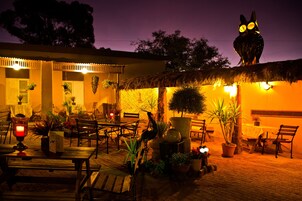 Un área de patio al aire libre con mobiliario de madera, plantas en macetas y una estructura de techo de paja.