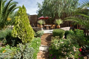 Un patio jardín con mesa y sillas de madera, y una sombrilla roja.