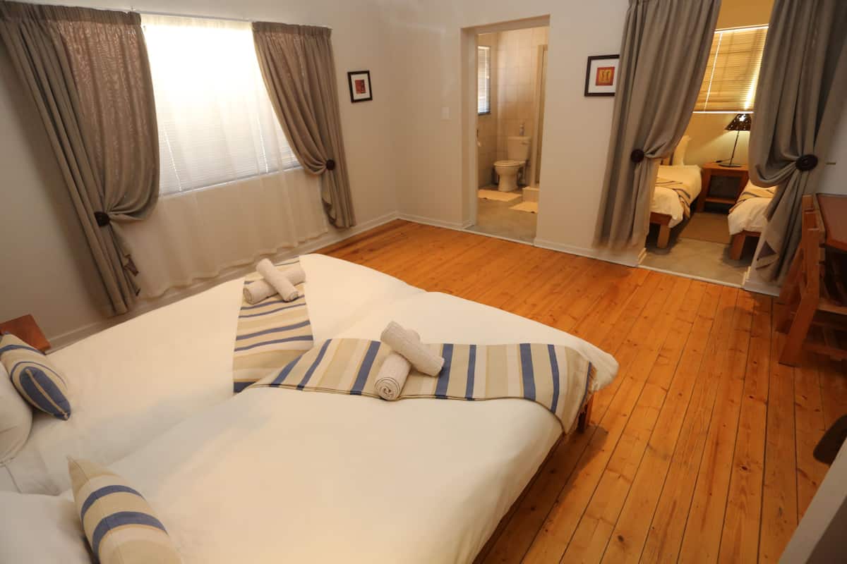 A bedroom with a large bed, wooden flooring, and a bathroom visible through an open door.