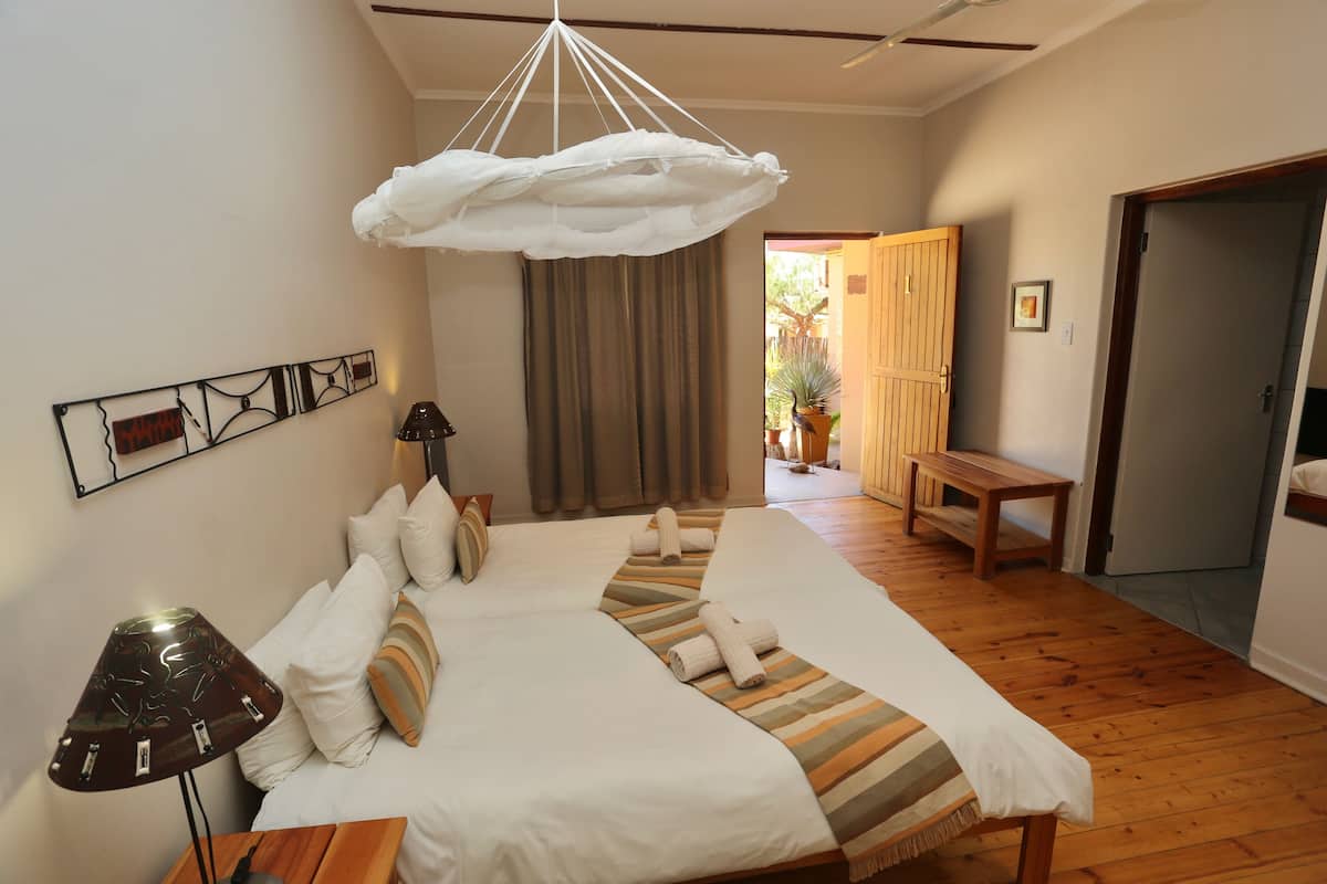 A bedroom with a large bed, a hanging light fixture, a bedside lamp, and a wooden bench in the corner.