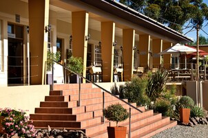 Un edificio con un área de estar al aire libre cubierta, una escalera que conduce a la entrada y varias plantas en macetas.