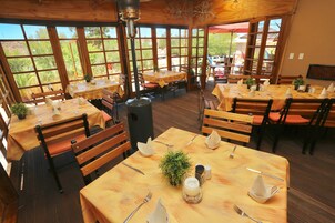 Un restaurante con mesas y sillas de madera, ventanas amplias y vistas al exterior.