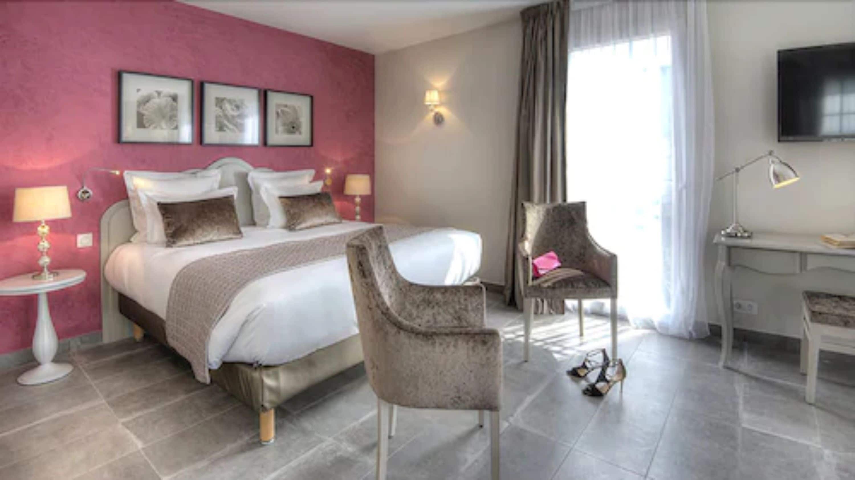 Une chambre d’hôtel avec un lit, deux chaises, un bureau, une télévision et une fenêtre avec des rideaux.