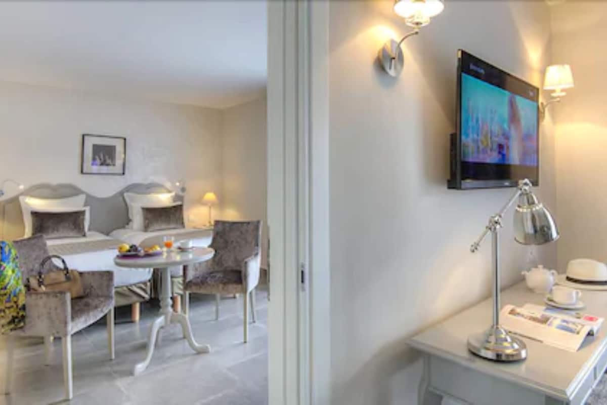 Et hotelværelse med seng, lille bord, fjernsyn og skrivebord med lampe og hat.