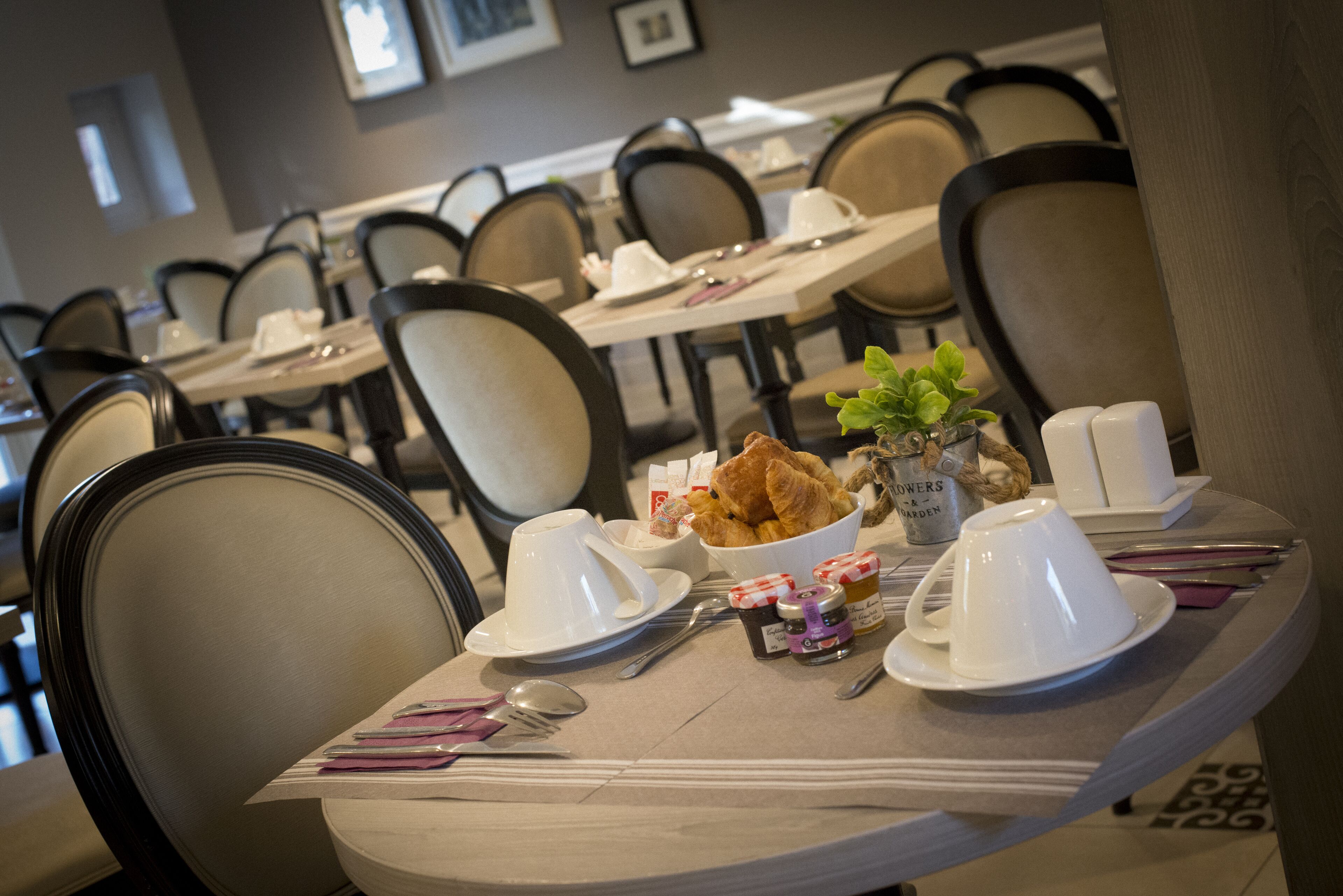 A dining area with tables set for breakfast, including croissants, coffee cups, and a small plant.
