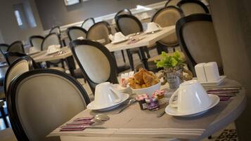 A dining area with tables set for breakfast, including croissants, coffee cups, and a small plant.