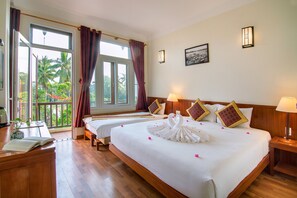 Une chambre d’hôtel avec un grand lit, deux tables de chevet, un bureau agrémenté d’une plante et une vue sur les palmiers par la fenêtre.