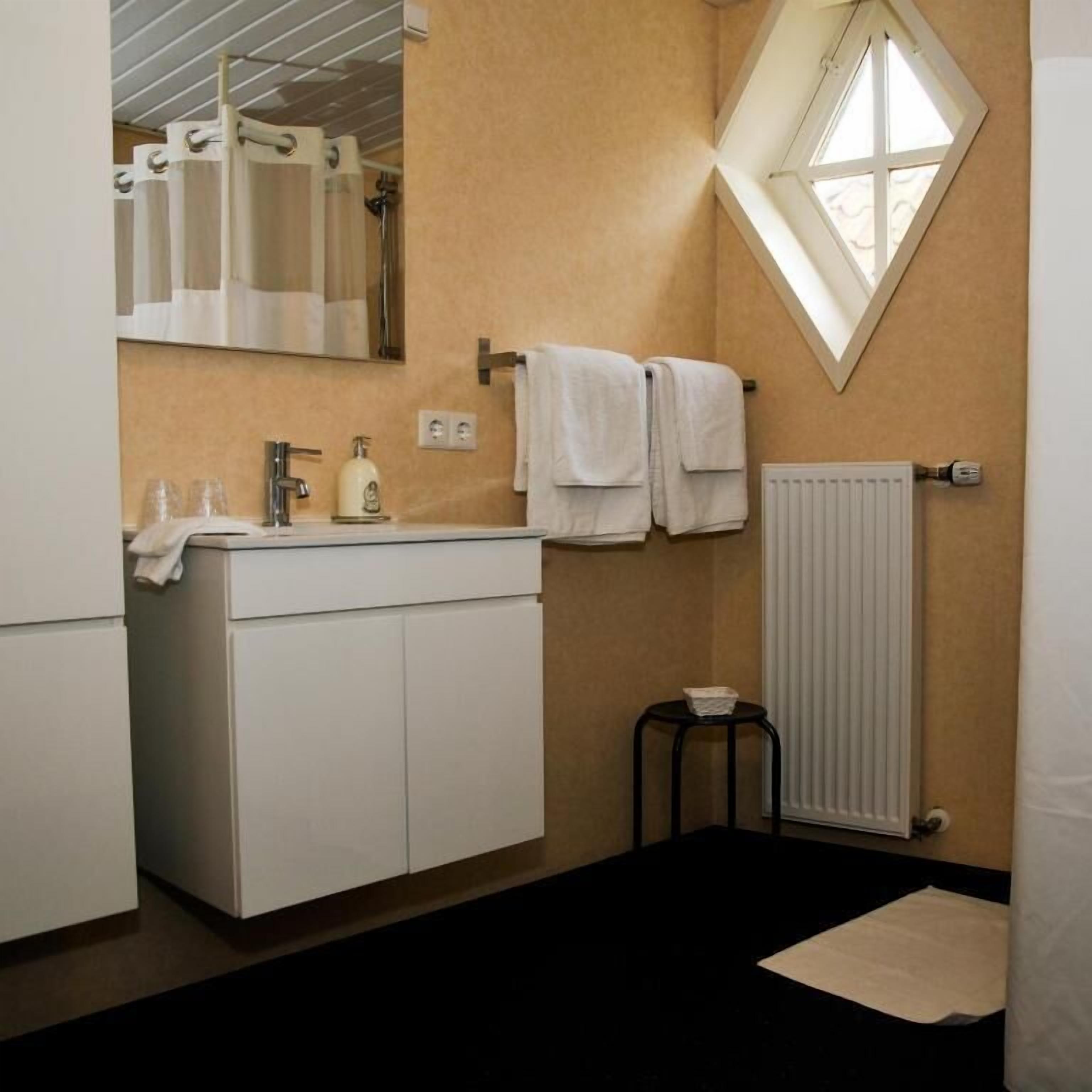 A bathroom with a white vanity, a mirror, a towel rack, a radiator, and a small stool.