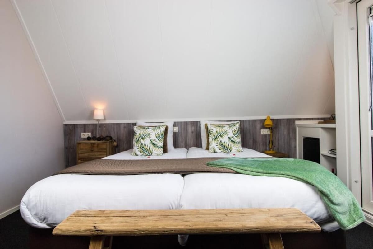 A bedroom with a bed, pillows, a bedside table, a lamp, and a bench.
