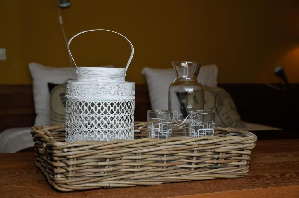 Een rieten mand met daarin een witte geweven houder, een glazen fles en enkele kleine glazen potjes.