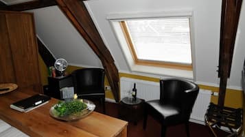 A room with a sloped ceiling, a skylight, a wooden table with a plant, two black chairs, and a radiator.