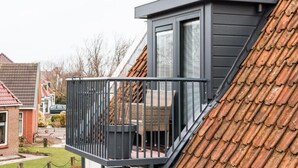A residential building with a sloped roof, a balcony with a metal railing, and a window with blinds. - Hotel Restaurant It Posthus (Burdaard)