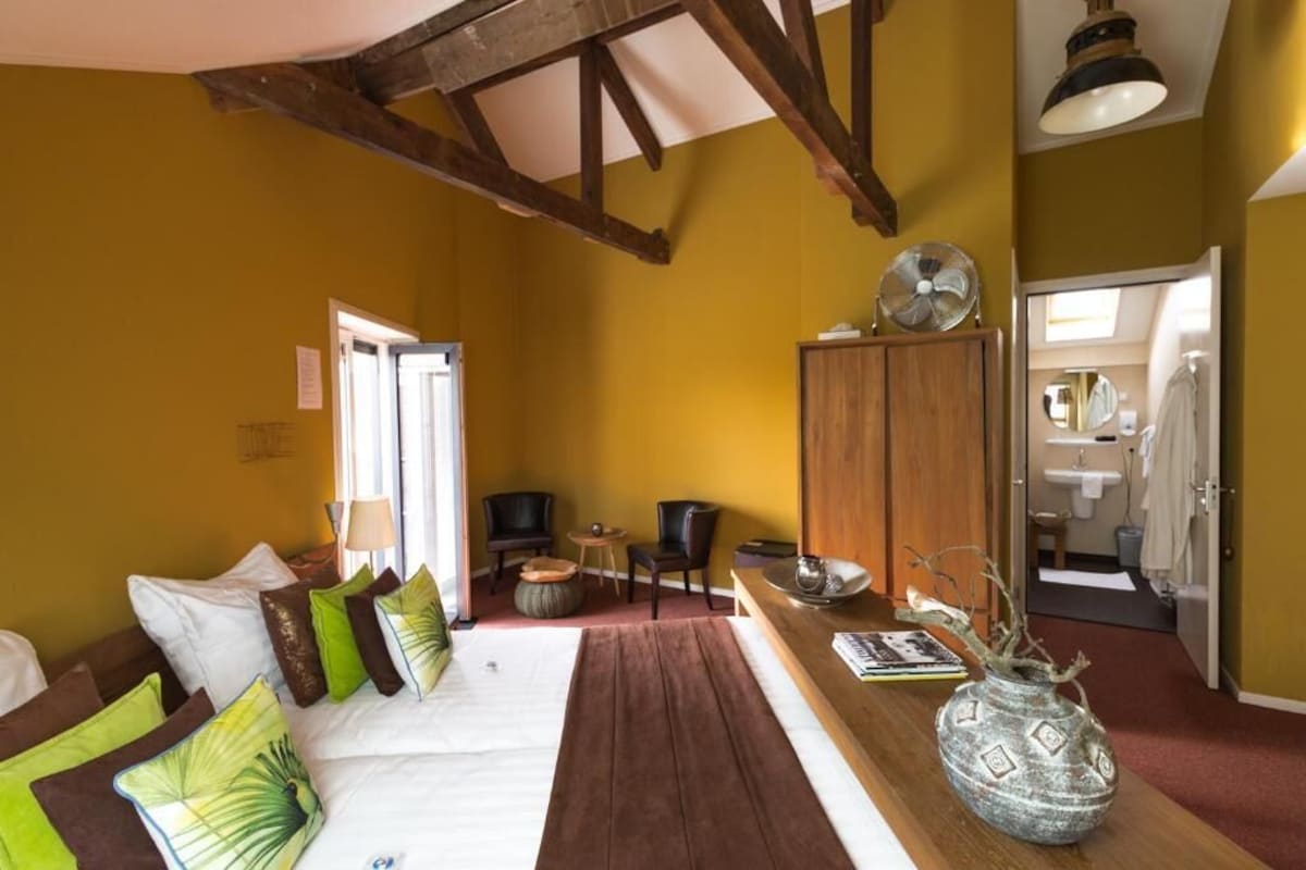 A room with a bed, a wooden cabinet, a fan, and a view into the bathroom.