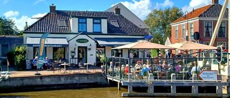 Un restaurante junto al río con terraza, un muelle y un edificio con un cartel que indica que es un hotel.