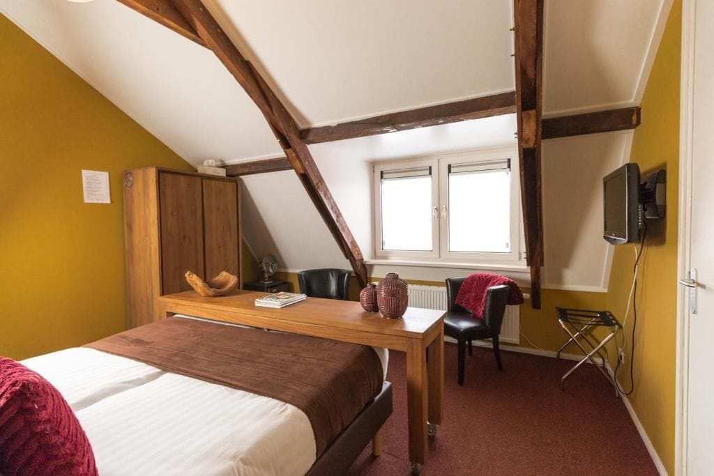 A bedroom with a bed, a wooden desk, a chair, a radiator, and a television.
