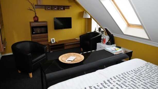 A room with a bed, a desk, a chair, a television, and a skylight. - Hotel Restaurant It Posthus (Burdaard)