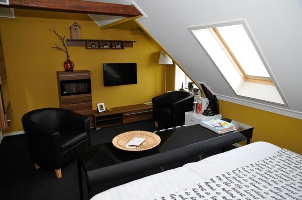 A room with a bed, a desk, a chair, a television, and a skylight.