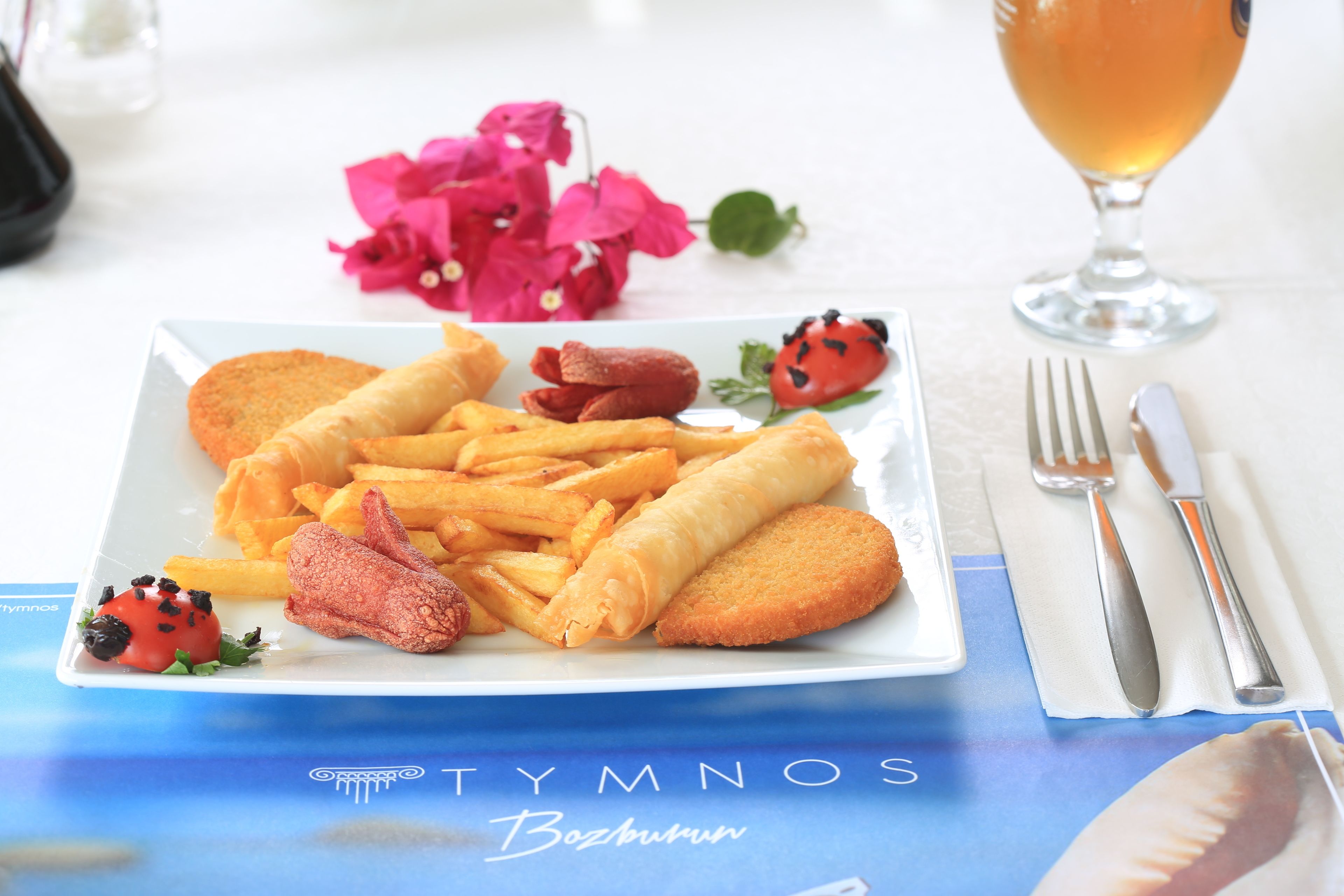 A plate of food with fries, spring rolls, and a small tomato garnish.