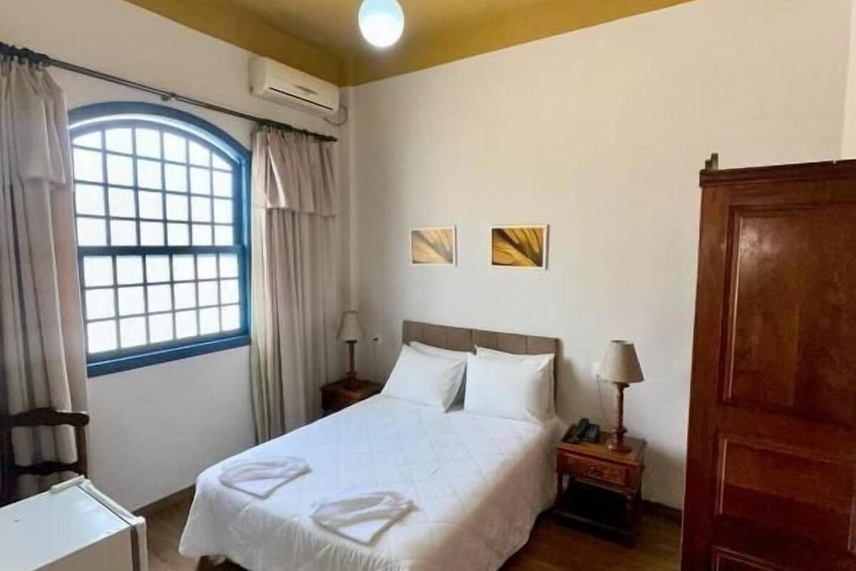 A hotel room with a bed, a desk, a wardrobe, and a window with curtains.