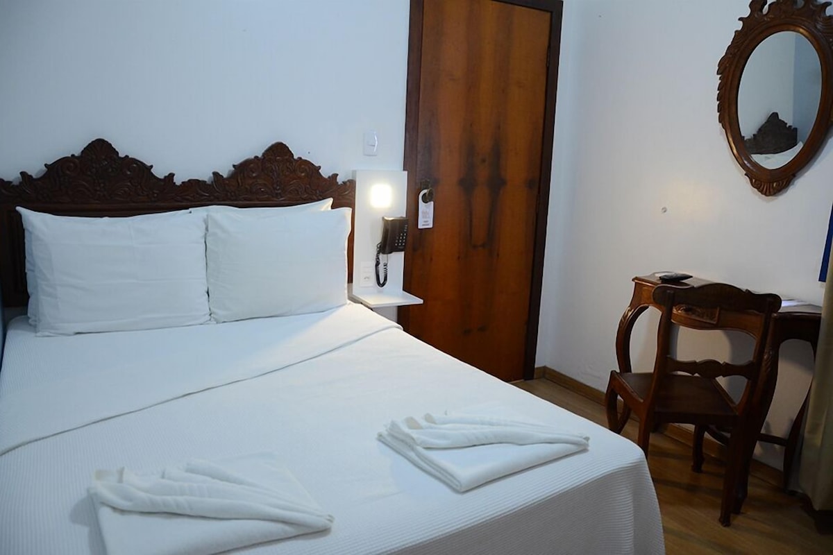 A neatly made bed with white linens, a wooden headboard, a bedside telephone, and a wooden chair.