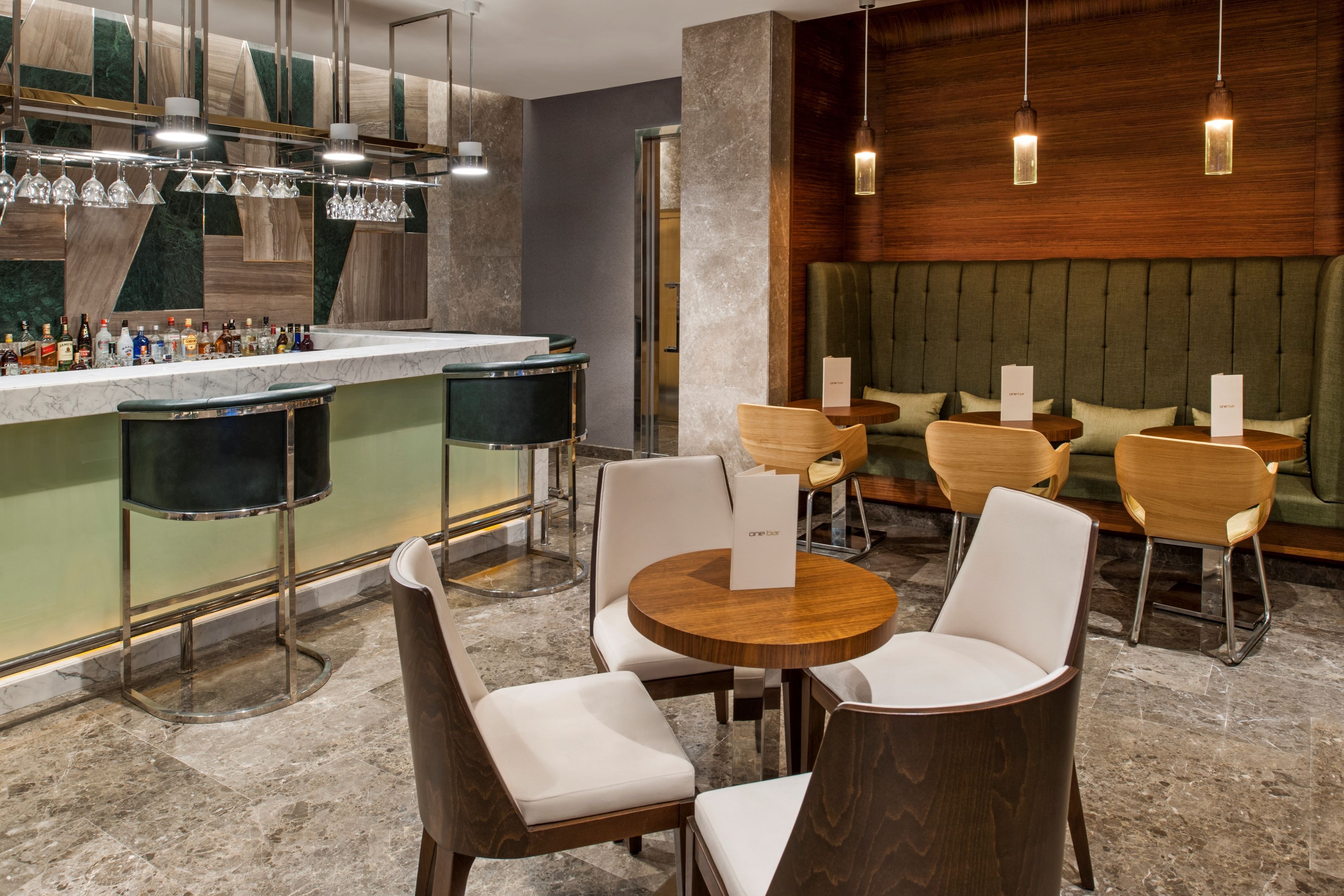 Un espace bar moderne doté d’un comptoir en marbre, de tabourets de bar et d’un coin salon avec des tables et des chaises rondes.