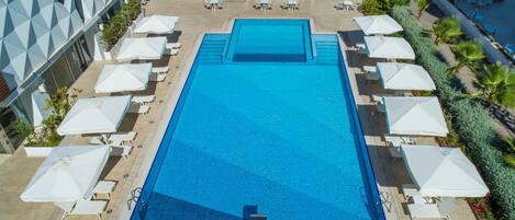 Une piscine rectangulaire avec un plongeoir au centre, entourée de chaises longues blanches et de parasols.