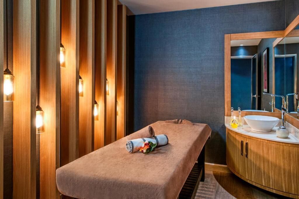 A massage room with a wooden panel wall, a massage table, and a wooden cabinet with a sink and mirror.