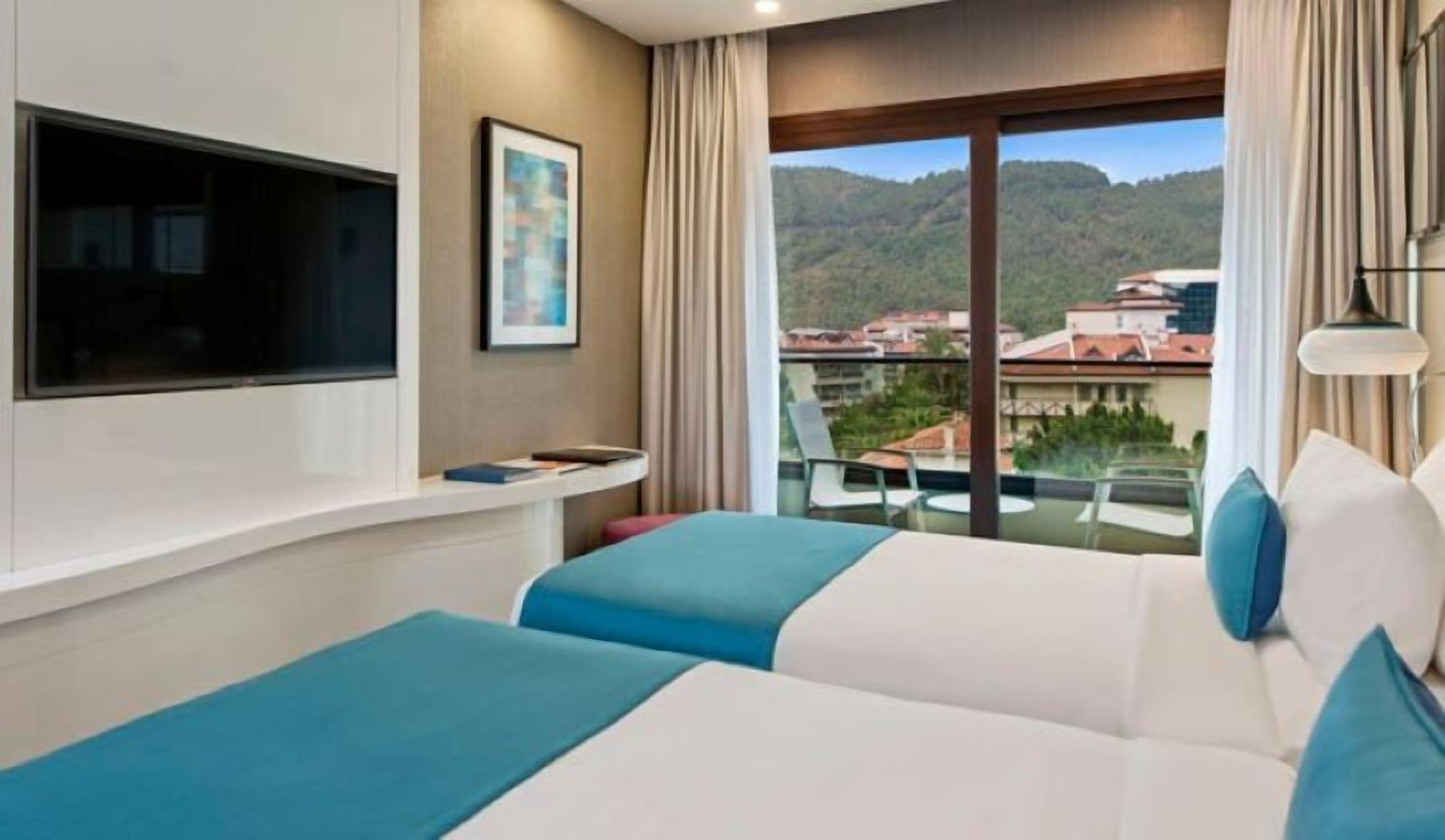 A hotel room with a balcony, a bed, a TV, and a painting.