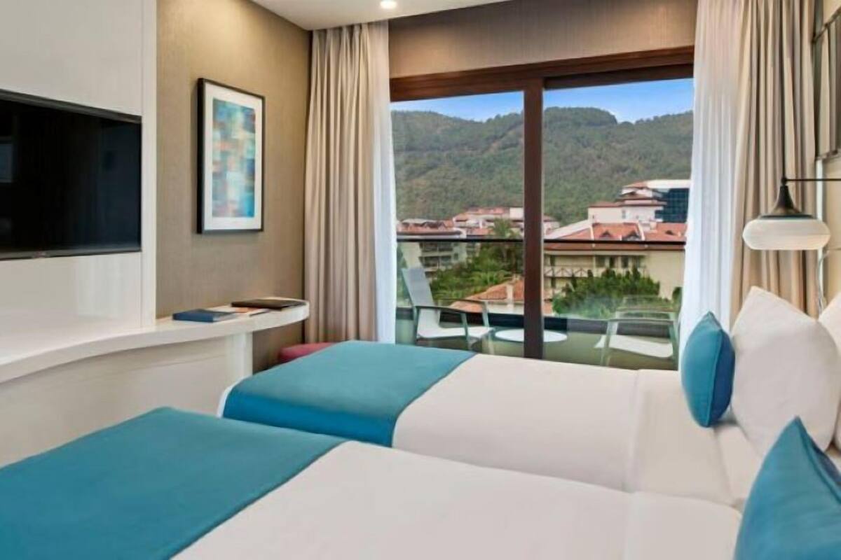 A hotel room with a balcony, a bed, a TV, and a painting.
