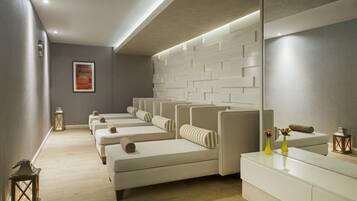 A spa room with multiple massage tables arranged in a row, a reception desk, and a wall-mounted mirror.