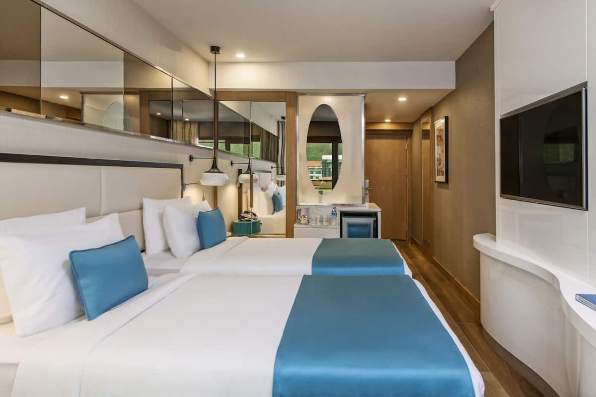 A hotel room with two beds, a TV, a desk, and a mirror.
