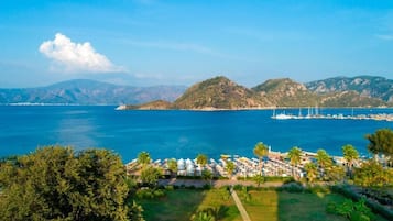 A coastal resort with a marina, lush greenery, and a mountainous backdrop.