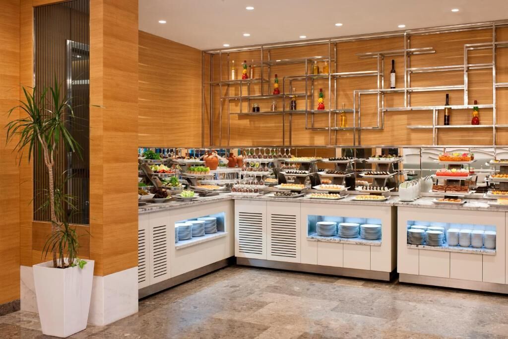 A buffet area with multiple food stations, a large potted plant, and a wooden wall with shelves holding bottles.