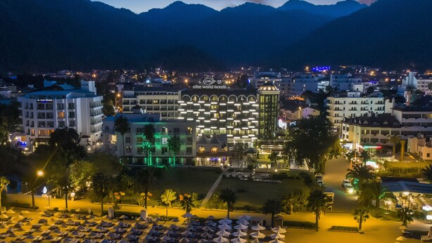 A hotel with multiple floors, a pool area with sun loungers, and a view of the surrounding cityscape and mountains. - Elite World Marmaris - Adult Only (Marmaris)
