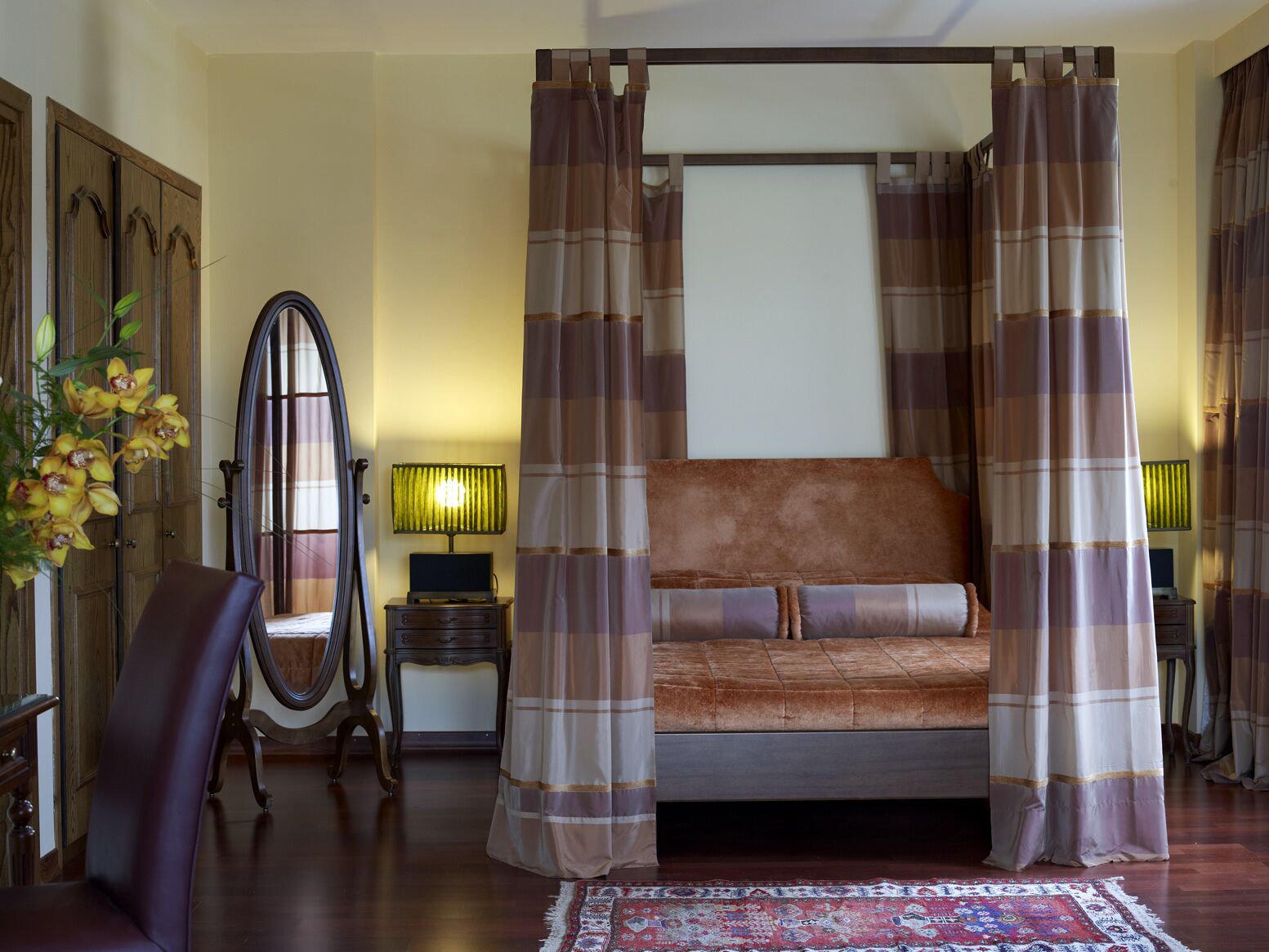 Un dormitorio con cama con dosel, una silla de madera, una lámpara y una planta decorativa.