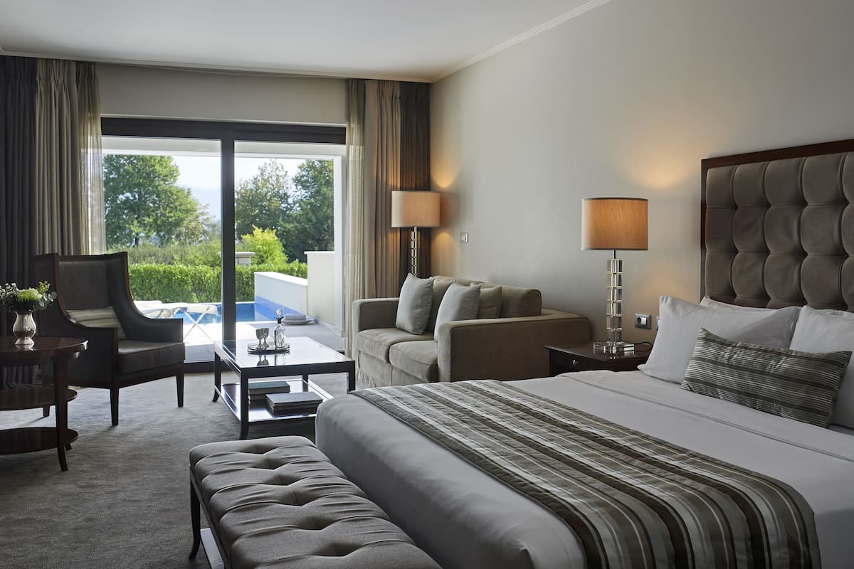 A hotel room with a large bed, a sofa, a chair, a desk, and a view of the outdoors.