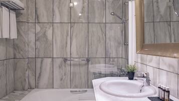 A bathroom with a bathtub, a shower, a sink, and a mirror.