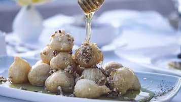A plate of round, golden-brown pastries with nuts and syrup, served on a white plate.