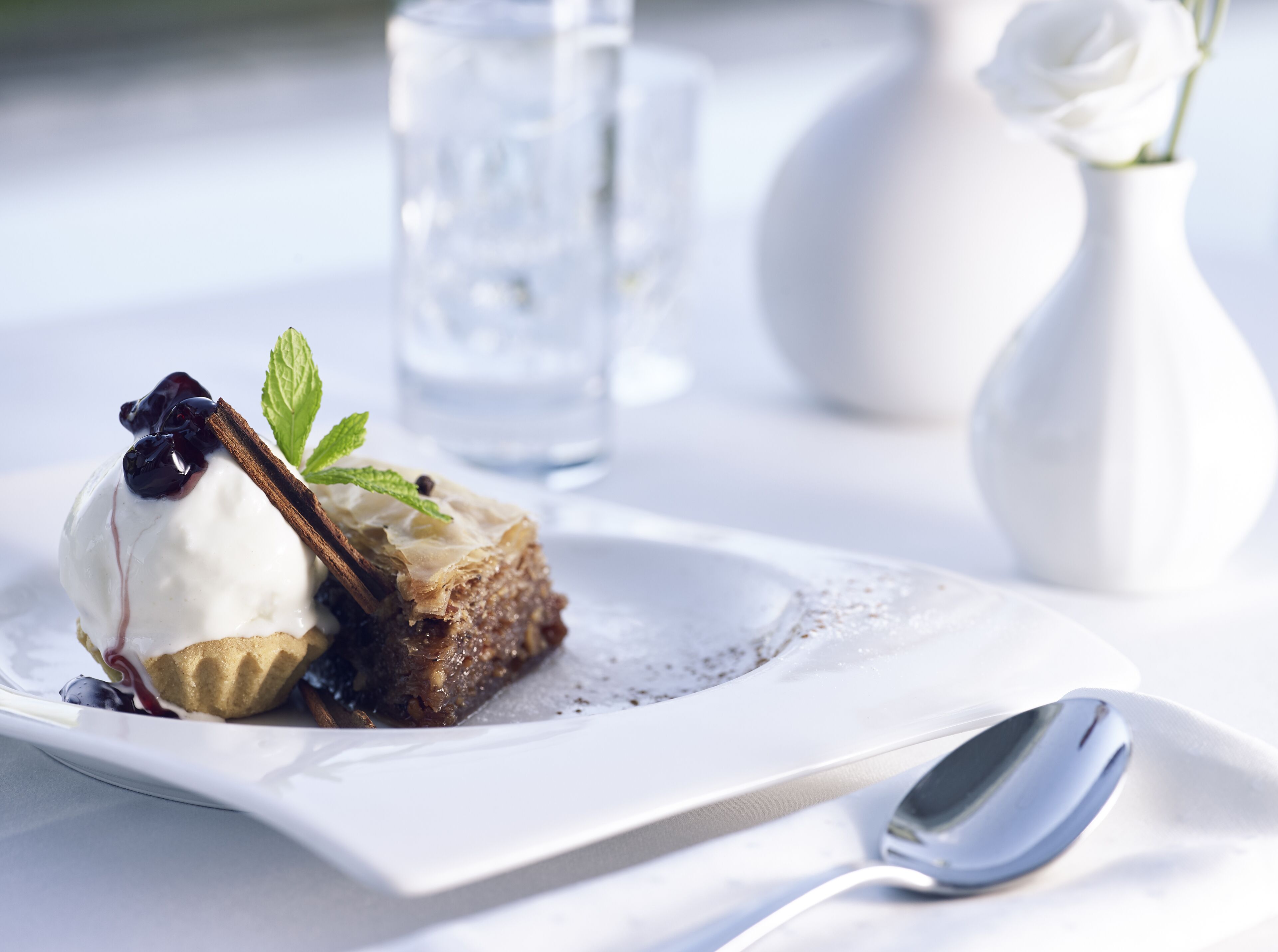 A dessert with a scoop of ice cream, a piece of cake, and a mint leaf on a white plate.