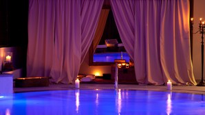 Zona de piscina con vistas a una habitación a través de cortinas translúcidas, velas y un candelabro.