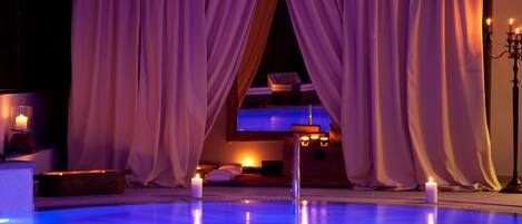 A pool area with a view of a room through sheer curtains, candles, and a candelabra.