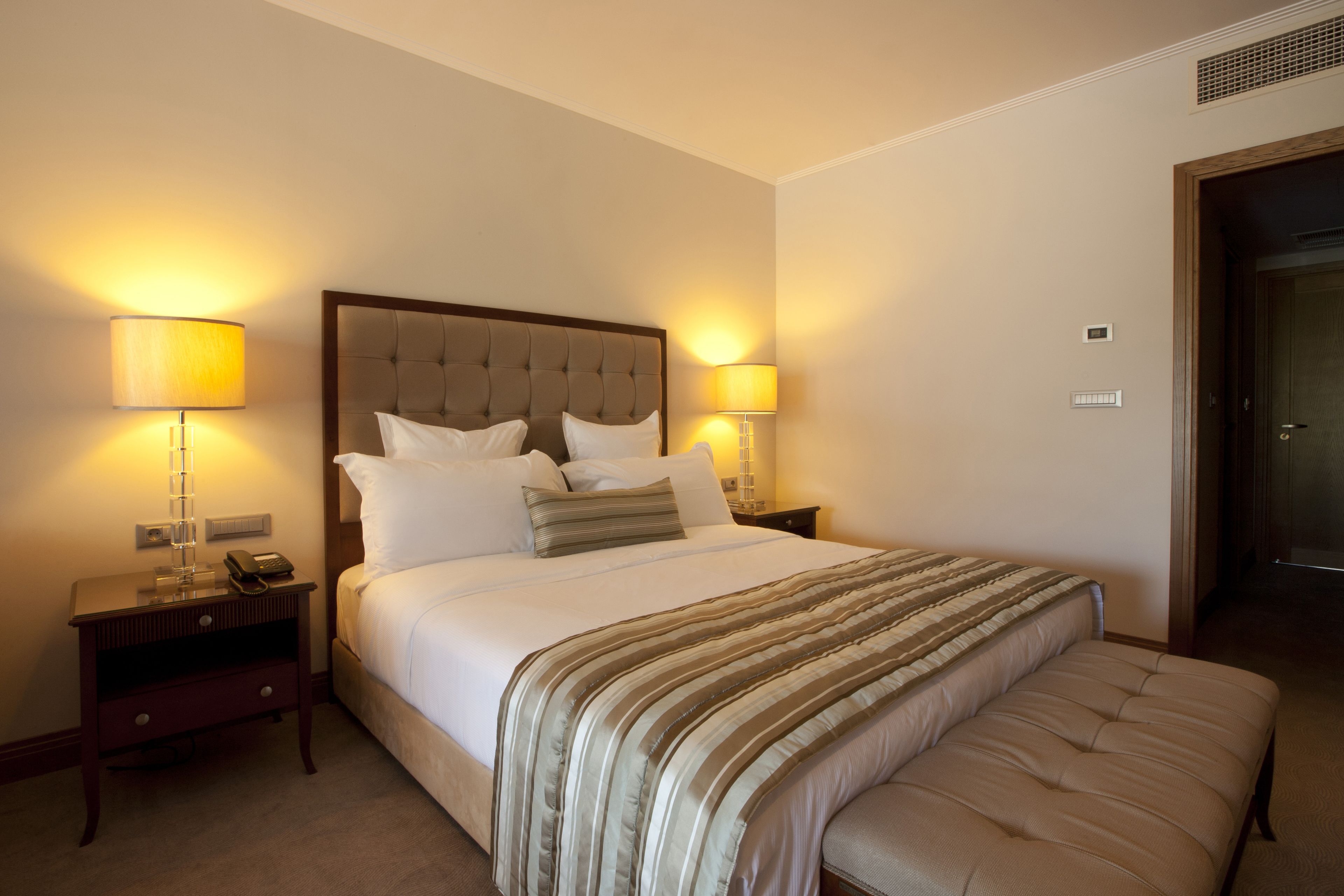 Une chambre d’hôtel avec un grand lit, deux lampes de chevet, une table de chevet avec un téléphone et une porte sur le côté droit.