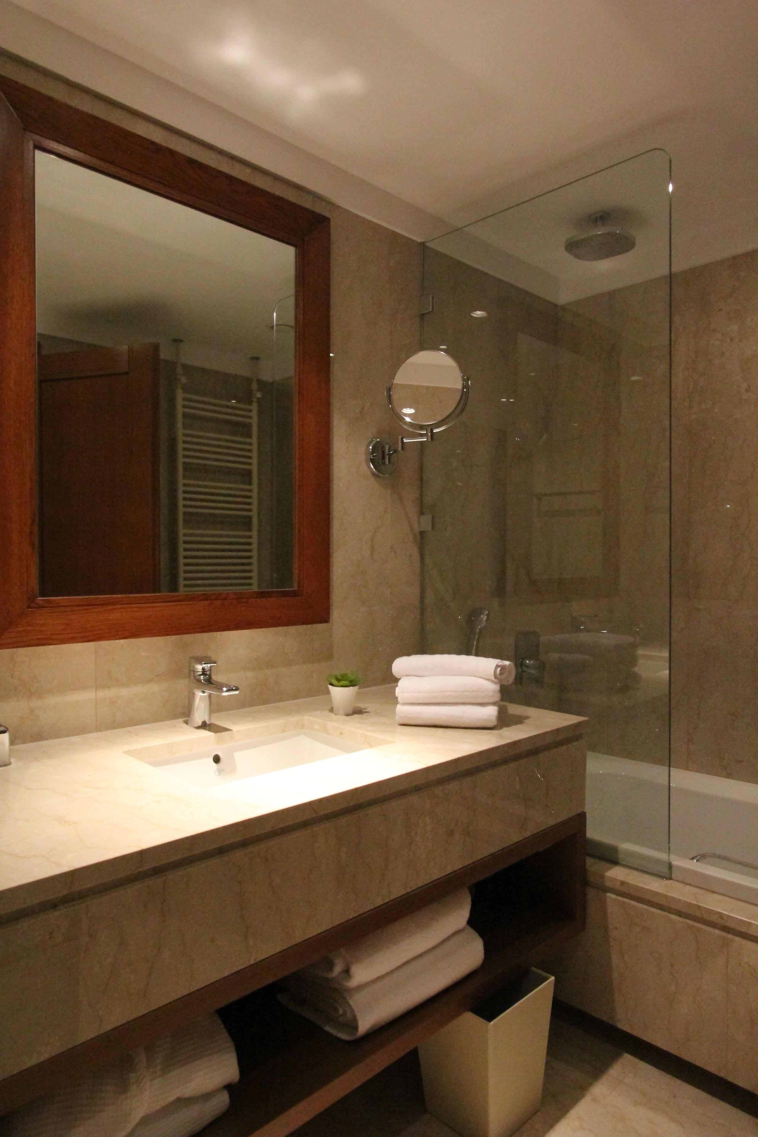 A bathroom with a marble sink, a large mirror, a glass-enclosed shower, and a towel rack.